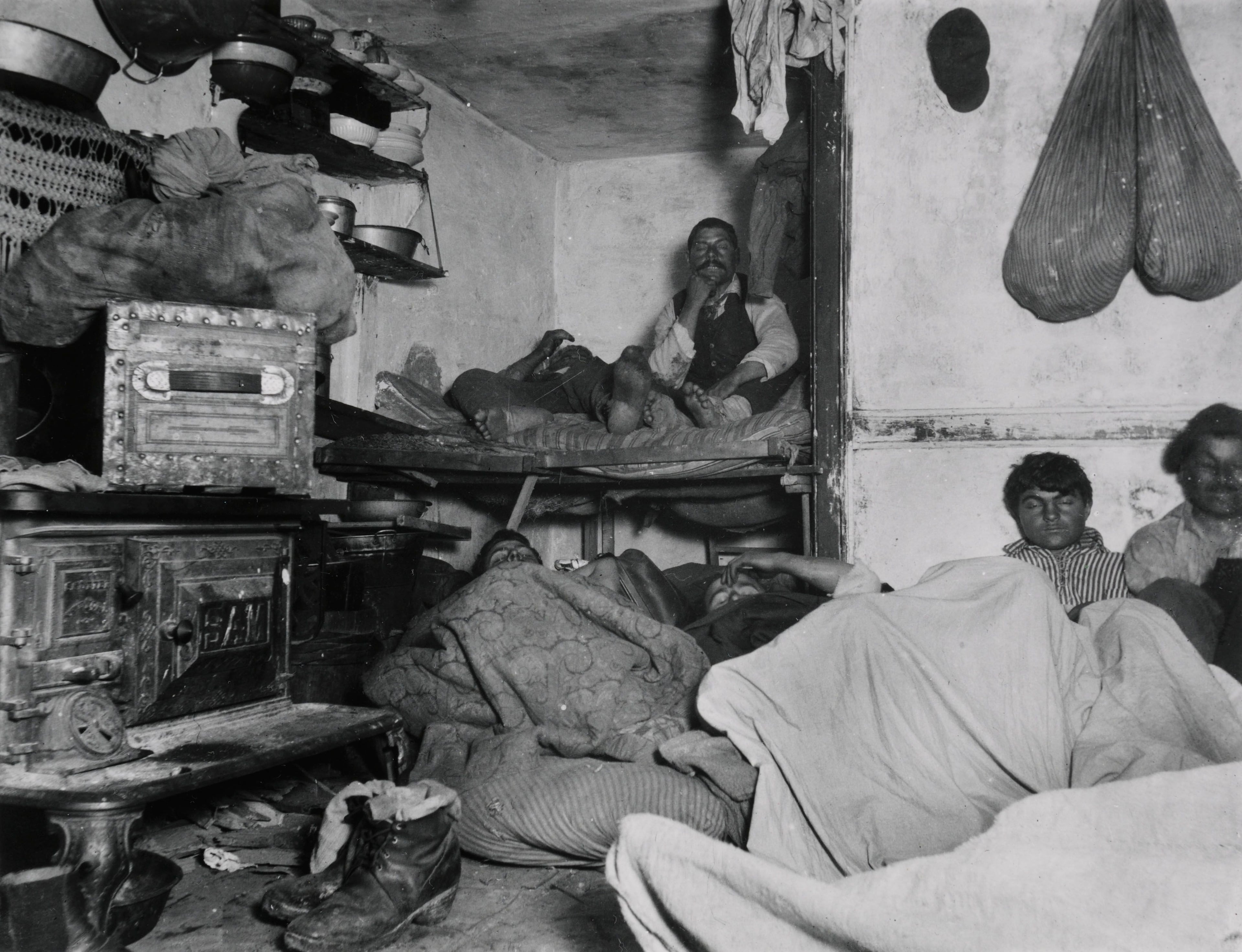 Black and white photograph of men sitting on their bunks in a crammed and dirty room