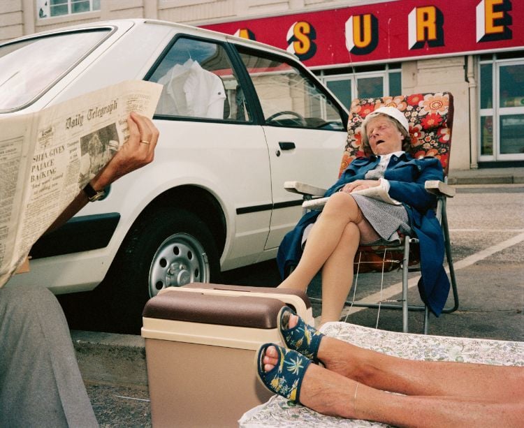 Photograph of a woman sleeping in a foldable chair in a parking lot